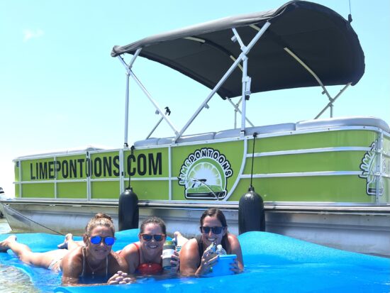 women laying on lilypad next to boat - lime pontoon rentals